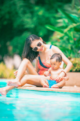 Asian mother and little son enjoying swimming in a swimming pool in summer vacation.