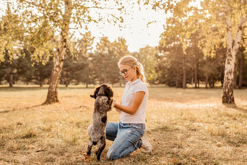 Teenager girl with glasses playing on grass with her little dog, brown cocker spaniel puppy, outdoors, in a park.