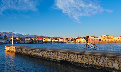 Early morning in Old Venetian port of Chania, Crete, Greece. Pier and bicycle in foreground. Quayside and Cretan mountains. Healthy lifestyle.