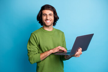 Photo of cheerful programmer guy hold netbook look camera wear glasses green pullover isolated blue color background