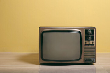 Retro old TV on floor in front of yellow concrete wall background.