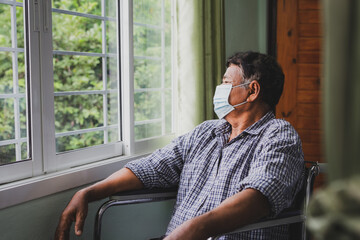 Elderly man sitting in wheelchair alone while looking out the window in the house.