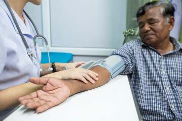 Young Asian nurse measuring blood pressure of elderly man, selective focus point