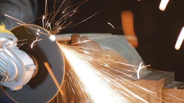 a worker cuts off metal fittings with a grinder, clamping them in a piece. The disc cuts the reinforcement first from below, then from above. Construction of metal structures. 4k