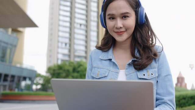Happy Young Asian women Use the laptop to Education or work in the city park. Meeting or study outdoors using free Wi-Fi internet access. Concept technology video conference