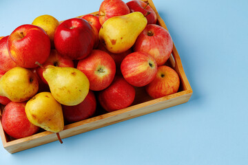 Wooden box with apples and pears on blue background