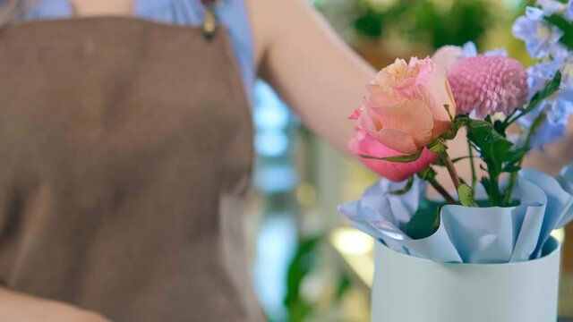 Professional florist hands prepare tender bouquet with blooming flowers in light blue hat box extreme close view slow motion