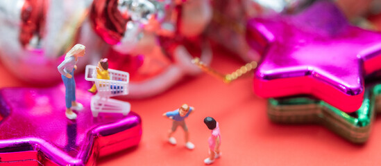 Miniature people with new year and Christmas holiday ornament in background. Holiday shopping concept is banner size