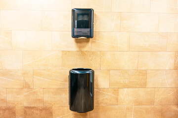 Paper towel black dispenser and a trash can at the bottom for used paper towels on the wall in a...