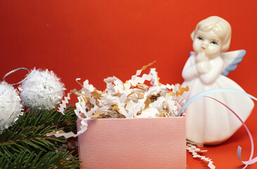 A gift box with confetti stands on a red blurry background with an angel. Christmas holiday background