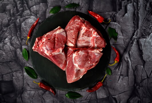 Fresh raw mutton shoulder meat isolated on black stone background with spices. Large piece of shmeat fillet or filet closeup