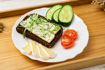 Blue cheese sandwich, brie cheese, cucumber and tomatoes on a plate on a wooden tray. Healthy food.