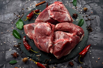 Fresh raw mutton shoulder meat isolated on black stone background with spices. Large piece of shmeat fillet or filet closeup