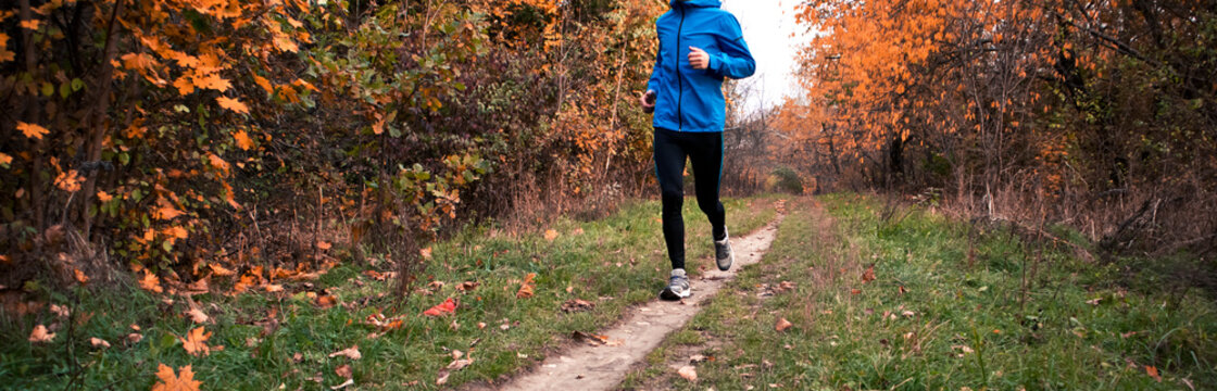 The young  man is running through the autumn park by pathway
