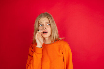 Shocked whisering secret. Portrait of young caucasian woman isolated on red studio background with copyspace. Beautiful female model. Concept of human emotions, facial expression, sales, ad, youth.