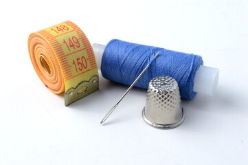 thimble, needle with thread and measuring tape on a white background .close-up.
