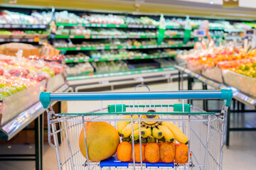 Shopping cart with many fruit in the supermarket when shopping and Blur abstract background of Fruit, Vegetable on shelves.