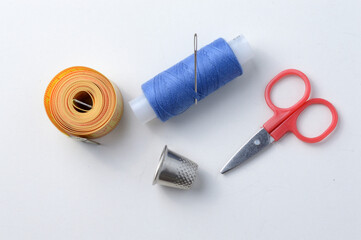 thimble, needle with spool of thread, scissors and measuring tape on a white background .close-up.