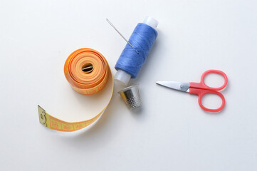 thimble, needle with spool of thread, scissors and measuring tape on a white background .close-up.