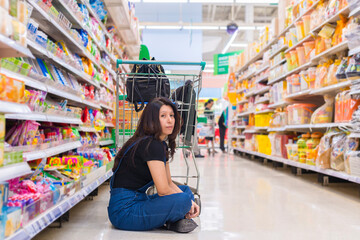Unhappy Asian woman with shopping trolley stressed and frustrated face because the product is very expensive at grocery store or Supermarket Aisle.