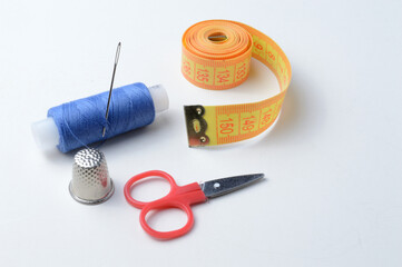 thimble, needle with spool of thread, scissors and measuring tape on a white background .close-up.