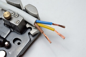 a wire stripper and a protected three-core wire on a white background. close-up