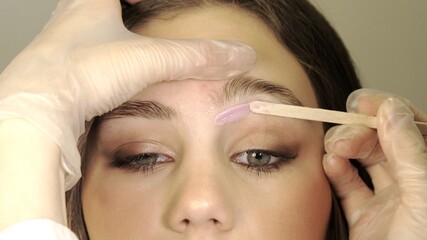 Correction of a shape of eyebrows with hot wax. Brow master applying wax on the eyebrow of female face of a brunette woman. Wax correction of the shape of the eyebrows. Beauty industry. 