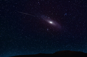 Beautiful Andromeda galaxy  on the starry sky over the hill silhouette. Night photography Astronomical wallpaper.