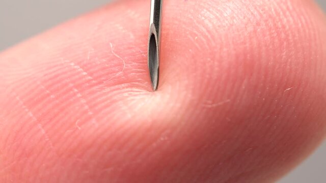 Finger touching medical syringe needle. Macro close up. Trypanophobia, extreme fear of injections or hypodermic needles. Dangerously close hand skin to the sharp needle. Phobias and traumas.