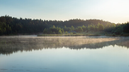 Summer landscape of Belarus. Beautiful sunrise over the lake. The sun's rays through the mist and trees.