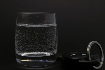 A glass of alcohol and car keys on a dark background