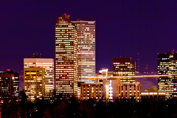 Fototapeta na wymiar Denver Night Construction Crane - The lights of a construction crane shine bright in the foreground as internally lit high rises of downtown Denver stand out against a night sky in Colorado