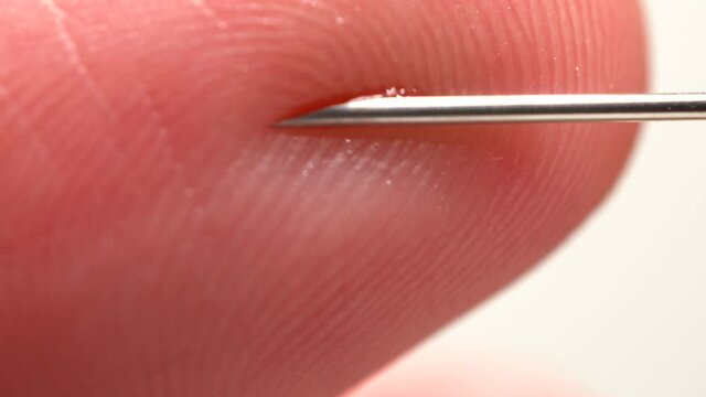 Finger touching medical syringe needle. Macro close up. Trypanophobia, extreme fear of injections or hypodermic needles. Dangerously close hand skin to the sharp needle. Phobias and traumas.