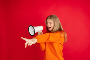 Shouting with megaphone, loudspeaker. Portrait of young woman isolated on red studio background with copyspace. Beautiful female model. Concept of human emotions, facial expression, sales, ad, youth.