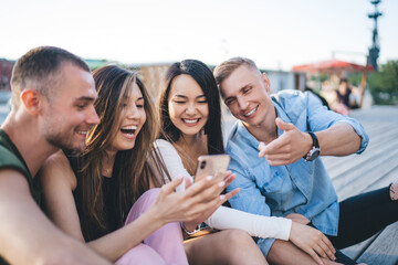 Laughing multiethnic friends browsing smartphone together