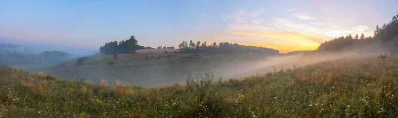 Beautiful summer hazy landscape with foggy hollow and green hills before the sunrise