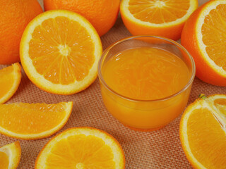 A cup of orange juice and many slided oranges on cutting board