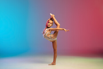 Energy. Little caucasian girl, rhytmic gymnast training, performing isolated on gradient blue-red studio background in neon. Graceful and flexible, strong child. Concept of sport, motion, action.