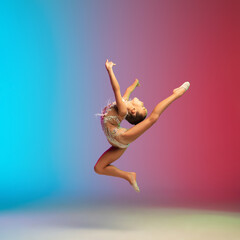 Fototapeta premium High jump. Little caucasian girl, rhytmic gymnast training, performing isolated on gradient blue-red studio background in neon. Graceful and flexible, strong child. Concept of sport, motion, action.