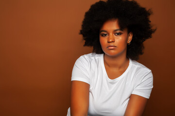 pretty young african american woman with curly hair posing cheerful gesturing on brown background, lifestyle people concept