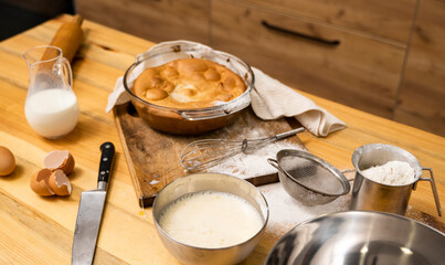 Tasty apple pie on a oaken wood table with a ingredients. Cooking a delicious apple pie on a kitchen in a loft style. Milk, eggs, sugar and a baked pie on a table. Home kitchen.
