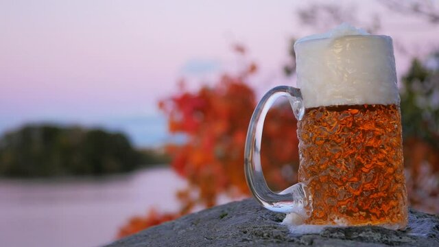 As the sun sets on the Swedish archipelago a cold lager beer is poured in to a rippled beer glass. The white foam pours over and slides down the side of the beer glass.