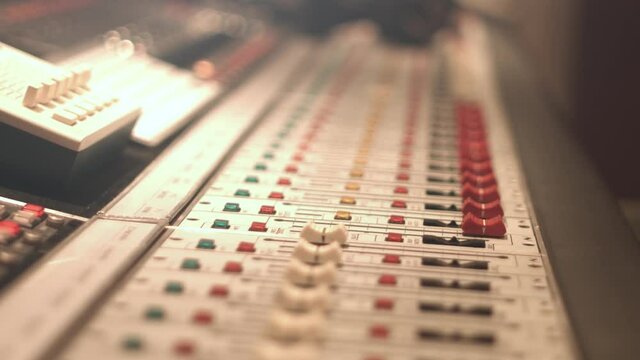 Close up of a 64 channel analog mixing table with red faders and knobs and headphones. Shot in 4K. Racking focus.