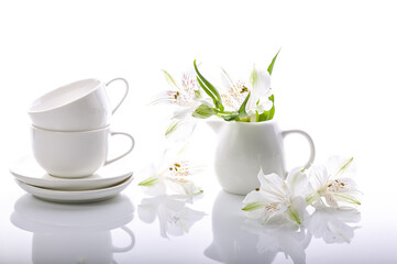 Obraz na płótnie Canvas Graceful white flowers and coffee set on a glossy background. Alstrameria, two cups and a milk jug. Still life