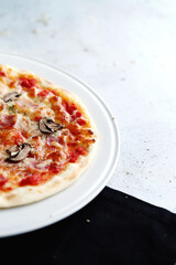 Partial view of ham and mushroom pizza on white plate and black napkin