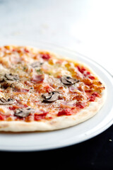 Partial view of pizza with ham and mushrooms on white plate in black and white background