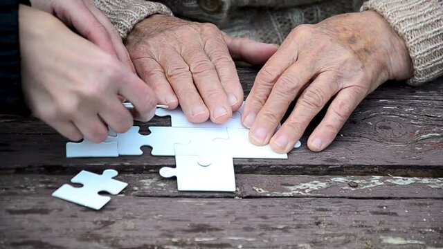 Granddaughter and grandmother are solving puzzles. The old grandmother is having fun with her family. An old grandmother develops memory and thinking by playing puzzles.