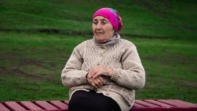 Lonely grandmother waiting on a bench in autumn weather A sad old grandmother sitting in thought. The sad face of the old grandmother. Social video of loneliness. Valuing parents concept