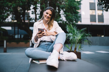 Portrait of cheerful woman in headphones smiling at camera while listening media content, happy hipster girl in electronic equipment enjoying leisure for using cellphone multimedia application