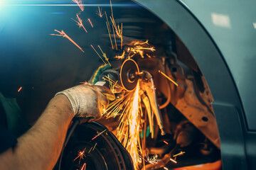Car repair, worker sawing rusted bolt with circular saw, sparks fly, auto repair shop.